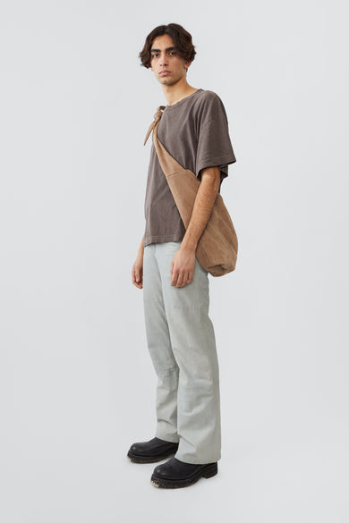 Boel beige suede crossbody sling bag  by Deadwood on male model with adjustable shoulder strap, zippered main compartment, and additional zip pocket. Made from upcycled suede leather and lined with recycled PET bottles.
