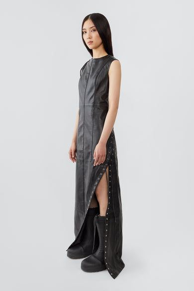 A female model wears the Ortem Maxi Dress in black, crafted from deadstock leather with a diagonal eyelet slit and adjustable leather laces, lined with recycled PET bottles.