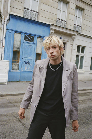 Male model wearing Stanley blazer in grey produced of upcycled cow lether featuring two bottons and duo waist pockets, black flynn pants made out of upcycled leather.