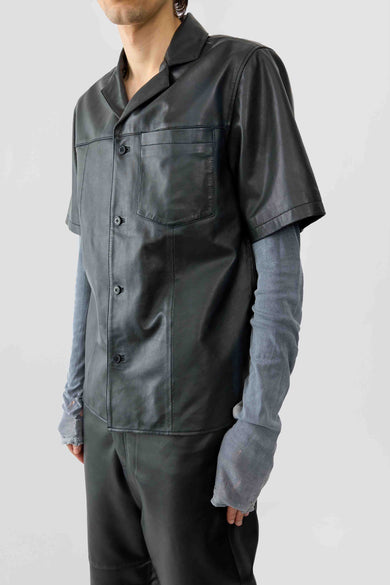 A person wearing a short sleeve black leather shirt with button-up collar and front pocket, paired with dark trousers.