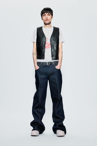 Person wearing a leather vest, white t-shirt, and raw blue denim jeans on a white background