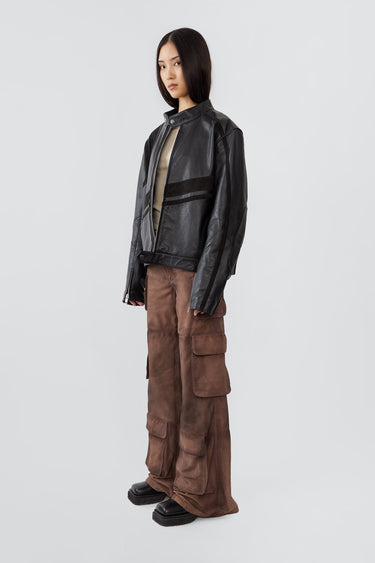 Side profile of model in Hiro black jacket, made from upcycled cow leather and goat suede, with a front zipper closure and ventilation hole.
