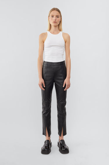 Front view of a model wearing high-waisted pants with a slim leg and ankle-length crop. The pants feature a split hem at the front and concealed side zip closure. Made from recycled leather with a lining made from recycled PET bottles.