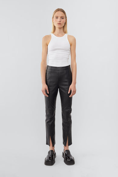 Front view of a model wearing high-waisted pants with a slim leg and ankle-length crop. The pants feature a split hem at the front and concealed side zip closure. Made from recycled leather with a lining made from recycled PET bottles.