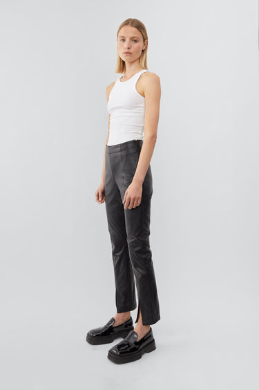 Side view of a model wearing high-waisted pants with a slim leg and ankle-length crop. The pants feature a split hem at the front and concealed side zip closure. Made from recycled leather with a lining made from recycled PET bottles.