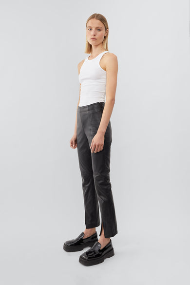 Side view of a model wearing high-waisted pants with a slim leg and ankle-length crop. The pants feature a split hem at the front and concealed side zip closure. Made from recycled leather with a lining made from recycled PET bottles.