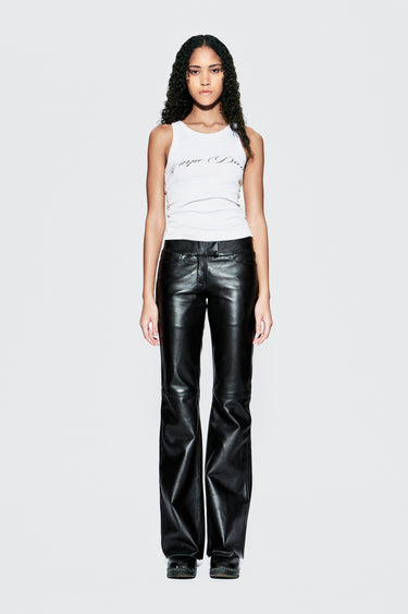 Model wearing a white tank top and black leather pants on a white background