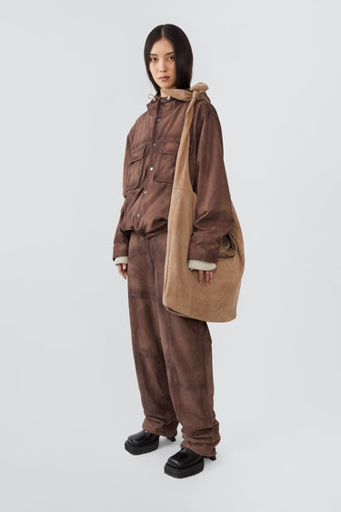 Boel beige suede crossbody sling bag  by Deadwood on female model with adjustable shoulder strap, zippered main compartment, and additional zip pocket. Made from upcycled suede leather and lined with recycled PET bottles.
