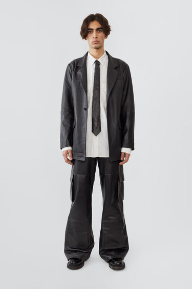 Model in Timo Tie by Deadwood, black leather tie made from upcycled lambskin with silver-tone logo detail.