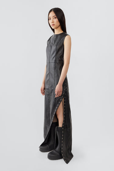 
A female model wears the Ortem Maxi Dress in black, crafted from deadstock leather with a diagonal eyelet slit and adjustable leather laces, lined with recycled PET bottles.