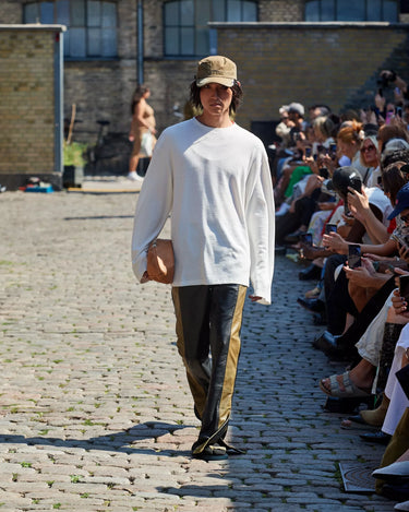 Male model on runway wearing white and black outfit from Deadwood Spring/Summer 2025 Collection during Copenhagen Fashion Week. The look features upcycled leather and recycled cotton, reflecting the brand’s commitment to sustainable fashion