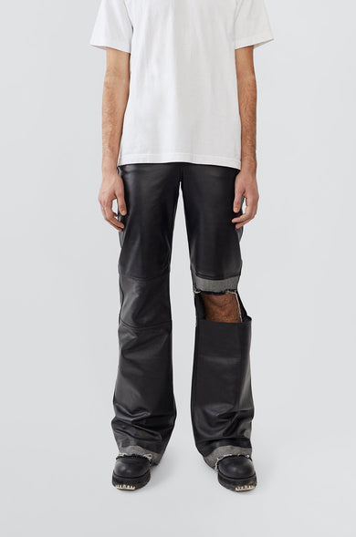Person wearing a white t-shirt and black leather pants with cut-out design on a light gray background