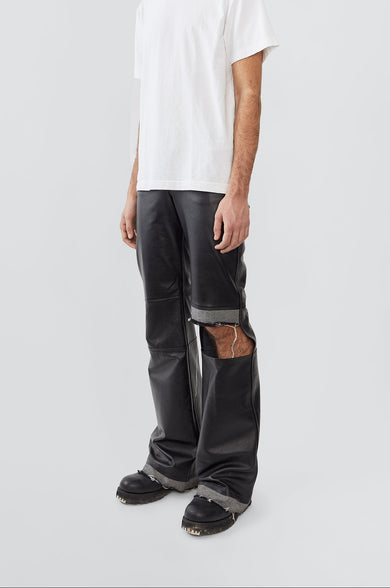 Person wearing a white t-shirt and black distressed leather pants with denim details on a light gray background