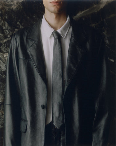 Close up of model in Timo Tie by Deadwood, black leather tie made from upcycled lambskin with silver-tone logo detail.