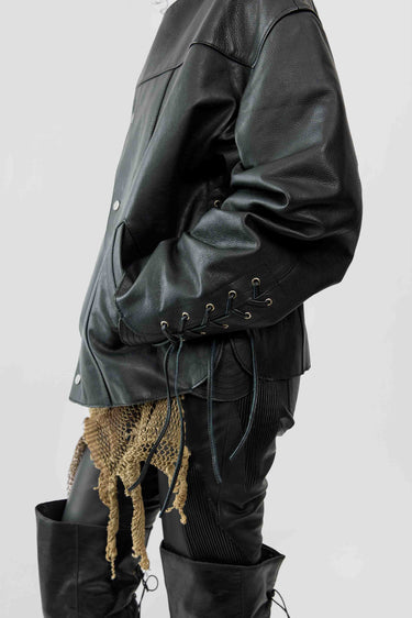 Side image of female model wearing Canoo Jacket in black upcycled leather, featuring drawstrings in cufs and duo waist pockets.