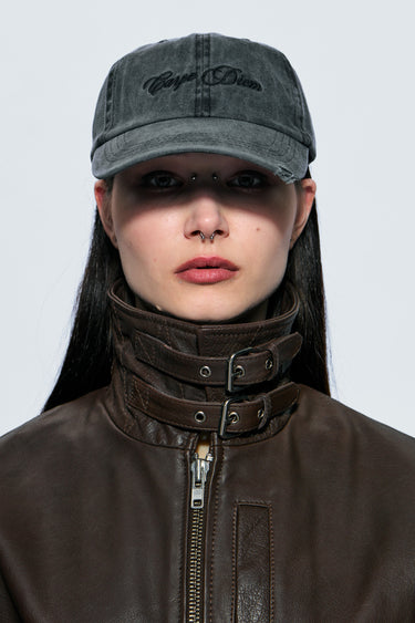 Model wearing a dark gray cap with 'Carpe Diem' branding and a brown leather jacket.