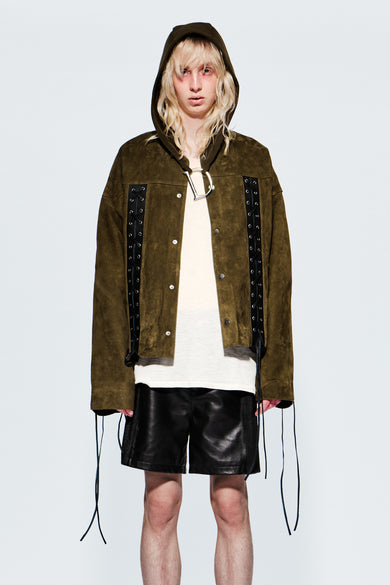 Person wearing a green suede jacket with black laced-up details and a green deadwood hood on a white background