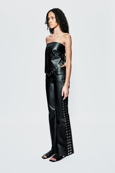 Side view of Dali black leather pants by Deadwood, featuring silver eyelets along the outer seams, flared legs, and mid-waisted fit. Made from upcycled leather.