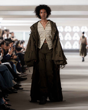 Model walking on Deadwood pre-spring 2026 runway show wearing a dark green outfit with a patterned shirt.