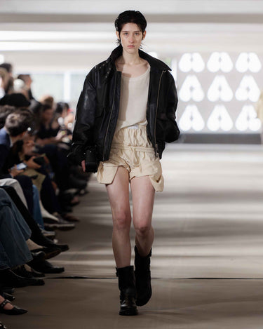 Model walking on Deadwood pre-spring 2026 runway show wearing a black leather jacket, beige top, and shorts.