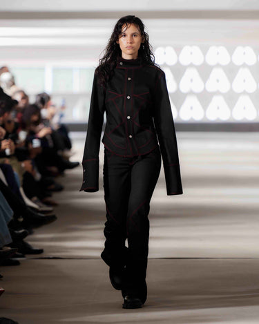 Model walking on Deadwood pre-spring 2026 runway show wearing a black denim outfit with red stitching.