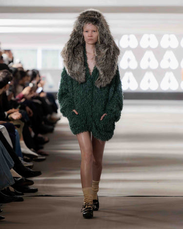 Model wearing a green knitted cardigan dress with a fur hood on Deadwood pre-spring 2026 runway show.