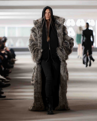 Model wearing a long fur coat on Deadwood pre-spring 2026 runway show with blurred audience in the background