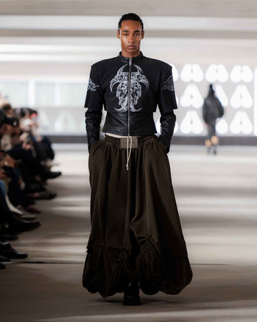 Male model wearing a leather jacket with vintage designs and oversized skirt on Deadwood pre-spring 2026 runway show. 