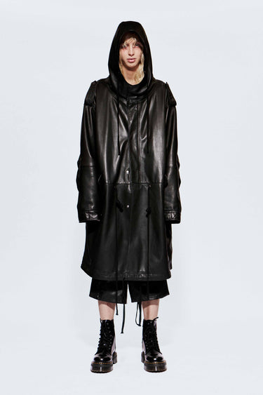 Male model wearing an oversized black recycled leather coat on a white background