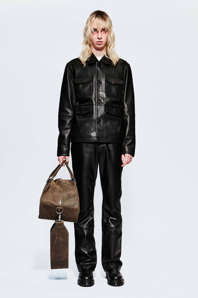 Front view of model wearing a black leather outfit holding a brown leather bag on a white background