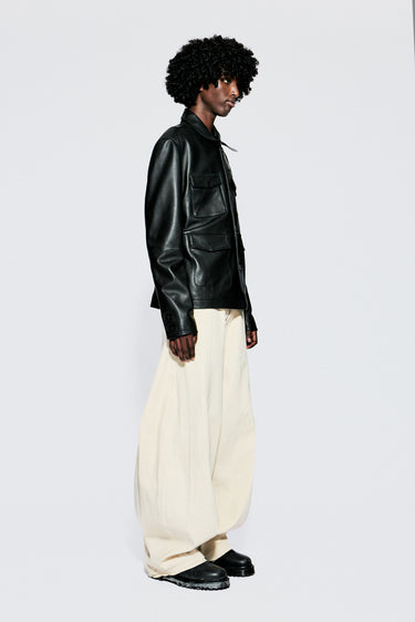 Side view of model wearing a black leather jacket and white pants on a white background