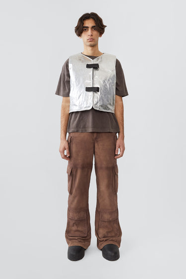 Picture of the front of an model wearing kapok vest, an silver vest with silver colored details and black buckles on the front. Made out of upcycled suede
