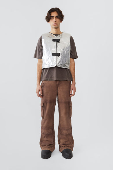Picture of the front of an model wearing kapok vest, an silver vest with silver colored details and black buckles on the front. Made out of upcycled suede