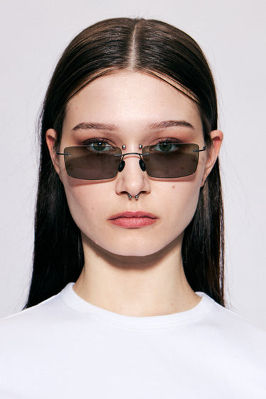 Model wearing Macrelaps by Deadwood, Rimless rectangular sunglasses with black lenses, matte black steel frame, engraved steel nose pads, and integrated steel temple tips.