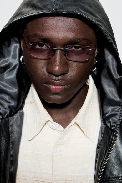 Male model wearing Macrelaps by Deadwood, Rimless rectangular sunglasses with pink lenses, matte black steel frame, engraved steel nose pads, and integrated steel temple tips.