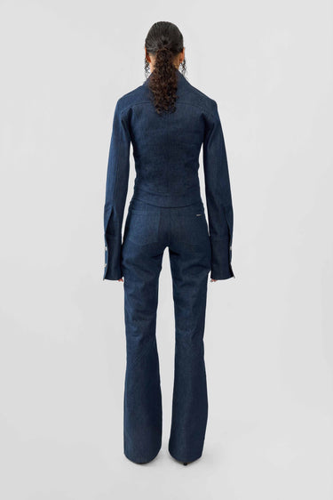 Back view of model wearing a blue raw denim outfit on a white background