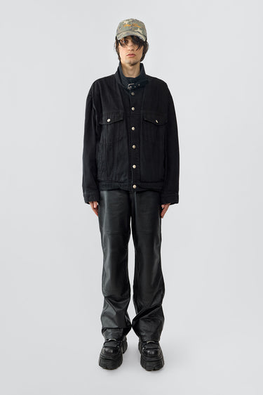 The Oracle Denim Jacket is an oversized black cotton denim jacket with steel jean buttons, flap chest pockets, and waist pockets. It features a strap and buckle at the collar for a uniform-inspired look, with dropped shoulders for a relaxed fit. Crafted with sustainable fashion in mind.