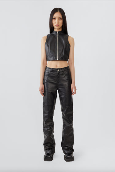 Front view of a female model wearing a cropped leather vest with a sleek central zipper and a short standing collar together with straight cut leather pants. Crafted from upcycled lambskin leather and lined with recycled PET bottles.