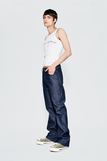 Model wearing a white tank top and blue raw denim jeans on a plain background