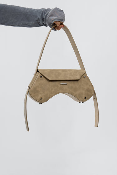 Model carrying stella bag in sand color. Crafted from upcycled leather and lined with cotton. The bag features an adjusteble strap and silver details