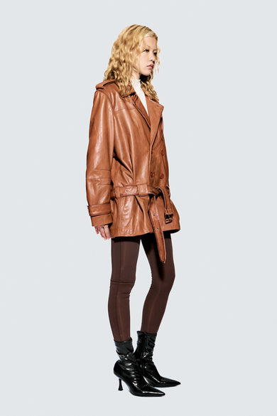 Model wearing a cognac colored leather coat on a light gray background