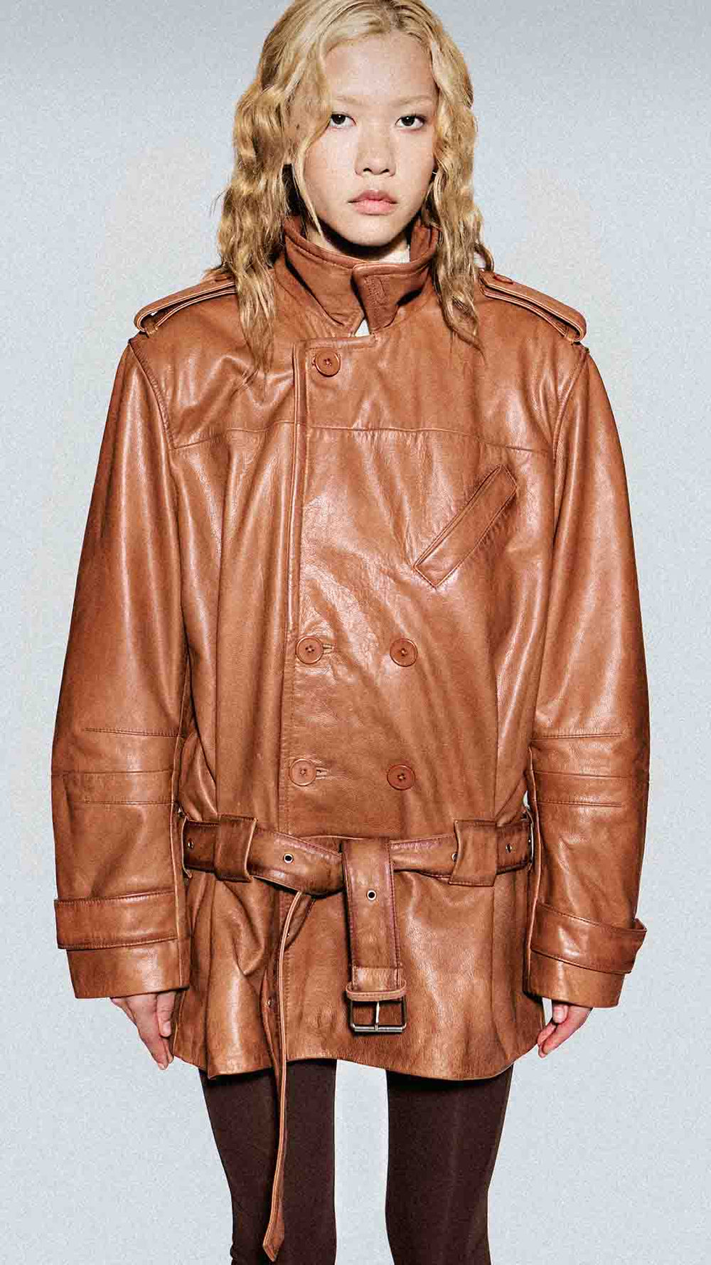 Model wearing a brown leather jacket on a plain background