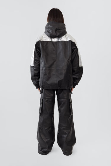 
Back view of model wearing the Tycho Jacket, a unique design crafted from upcycled leather and recycled aluminum-coated polyester. Features an orange lining, hood, drawstring hem, and multiple pockets.