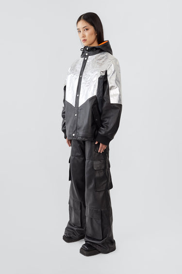 side view of model wearing the Tycho Jacket, a unique design crafted from upcycled leather and recycled aluminum-coated polyester. Features an orange lining, hood, drawstring hem, and multiple pockets.