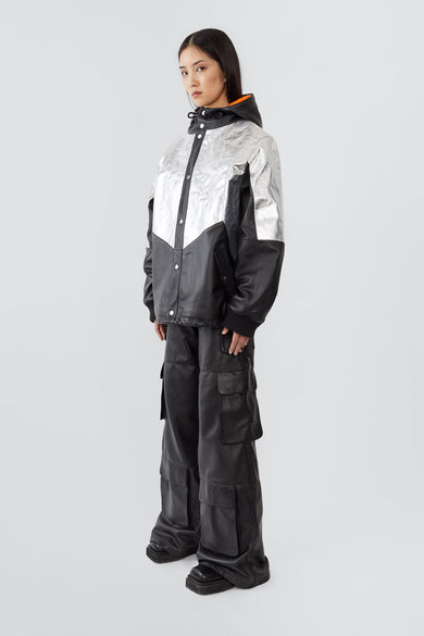 side view of model wearing the Tycho Jacket, a unique design crafted from upcycled leather and recycled aluminum-coated polyester. Features an orange lining, hood, drawstring hem, and multiple pockets.