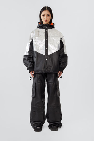 Front view of model wearing the Tycho Jacket, a unique design crafted from upcycled leather and recycled aluminum-coated polyester. Features an orange lining, hood, drawstring hem, and multiple pockets.