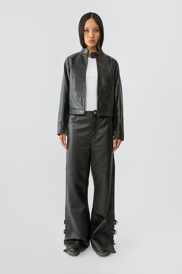 Model in Velar Jacket in black. 
Velar is a leather jacket with a straight silhouette and racer-inspired design. It features a center-front zipper, zipper slits at the cuffs, and an overlapping button closure at the collar. Made from upcycled grain cow leather with a recycled PET bottle lining.