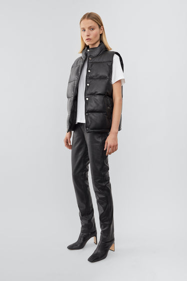 Model wearing Deadwood black down-free recycled leather puffer vest with push button closure at center front. Waist pockets and a drawstring at the hem. 