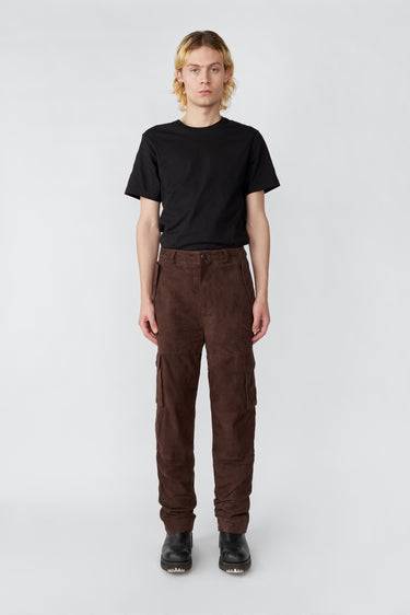 Model wearing brown Deadwood straight cut cargo pants with slightly dropped crotch, zip fly and workwear-inspired double waist pockets and leg pockets. One 32” length fits all. Made from recycled suede. 