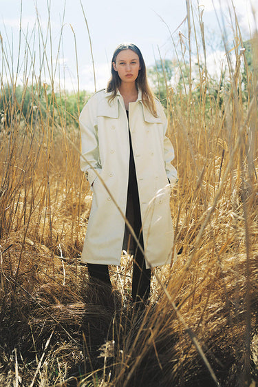 Model wearing Deadwood military-inspired trench coat in vegan cactus leather with belt, flap yokes at shoulders and back, and slit at bottom hem.